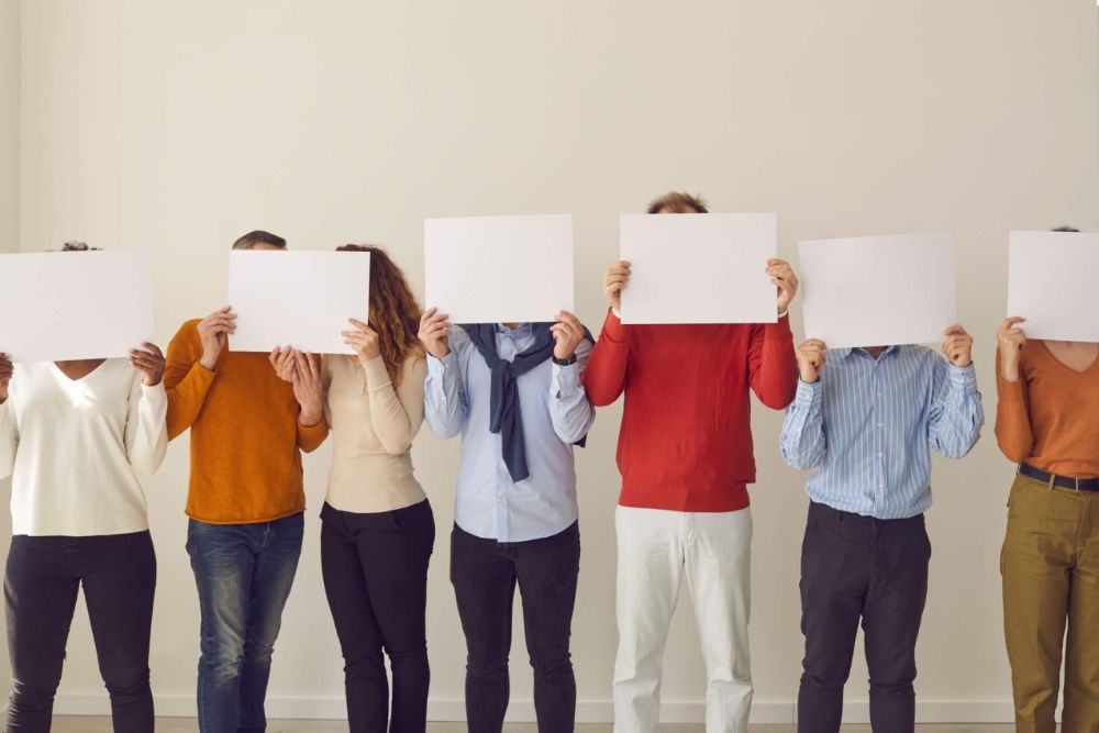 A row of people standing in a line holding paper over their faces.