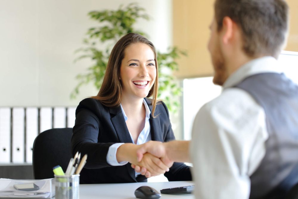 A job candidate shaking hands with an interviewer while sitting across from each other at a desk