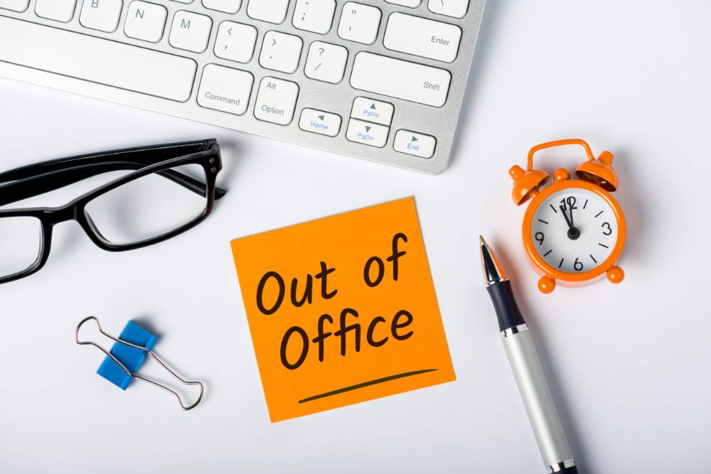 An overhead view of someone's desk with a sticky note saying out of office.