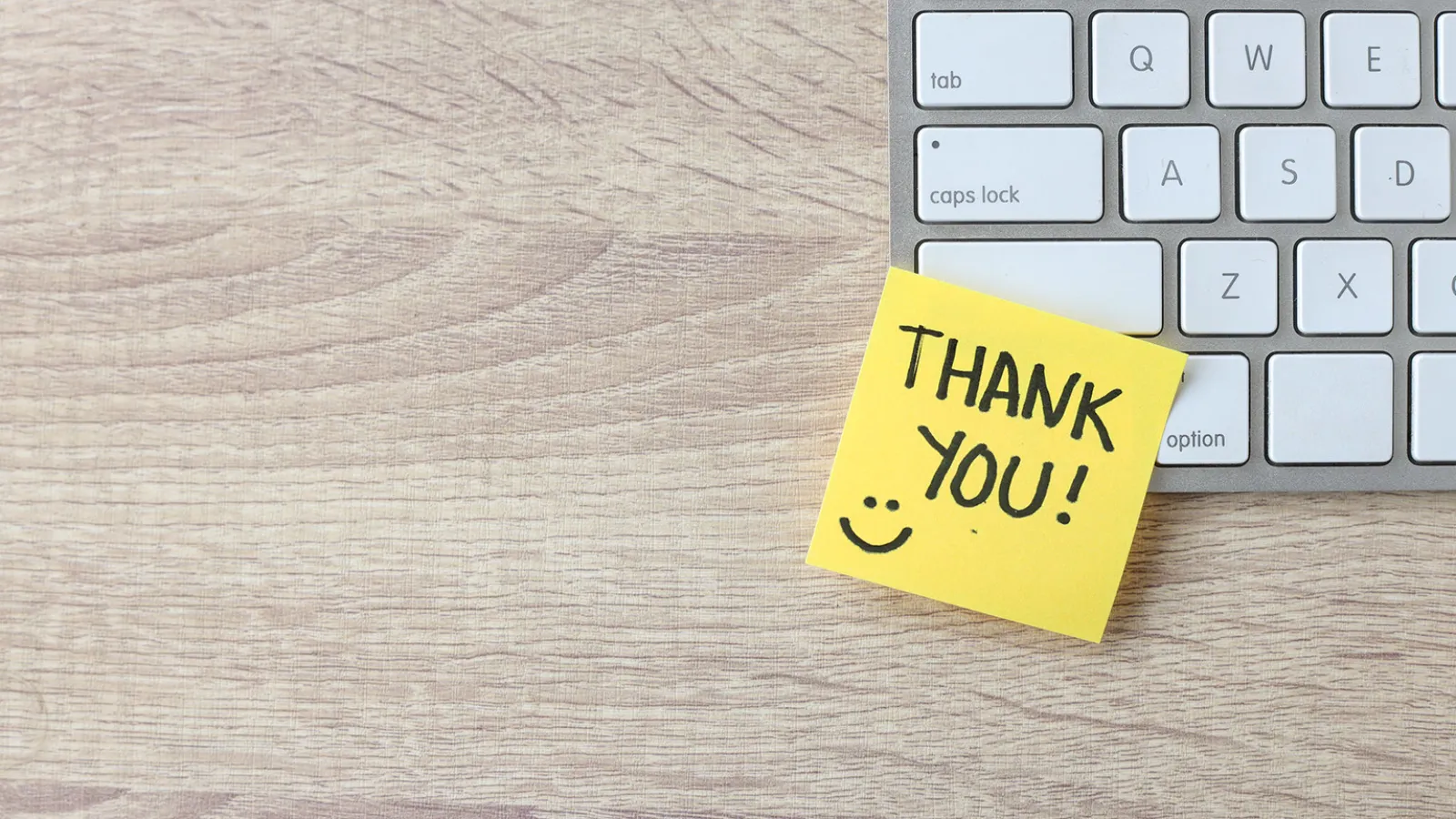 Photo of a computer keyboard with a yellow sticky note with the words thank you written on it.