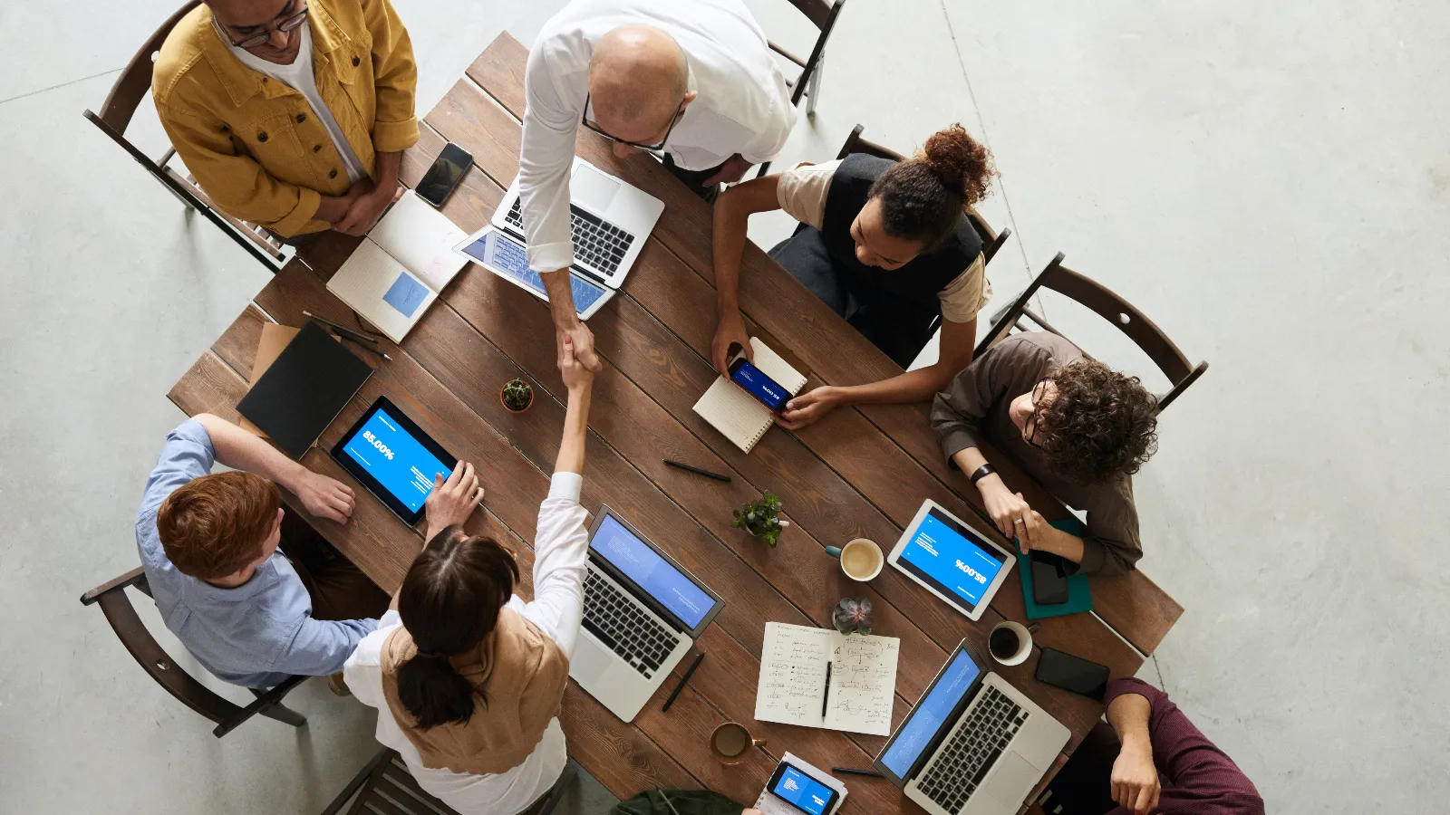 Overhead photo of a work team at a table. One person is shaking another's hand while everyone else sits.