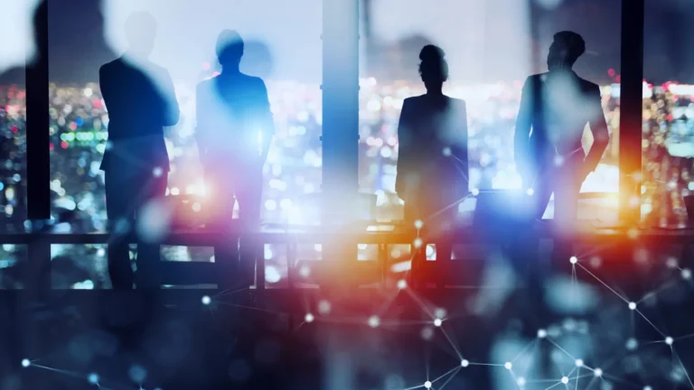 Silhouette photo of four professional people looking out a window at city scape.