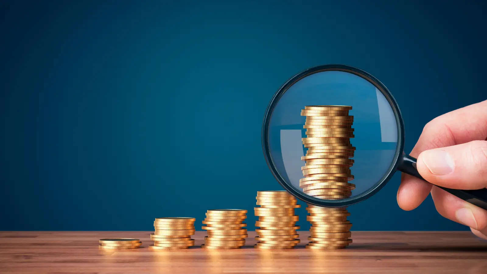 Five stacks of coins, increasing in height with a magnifying glass on the tallest stack.