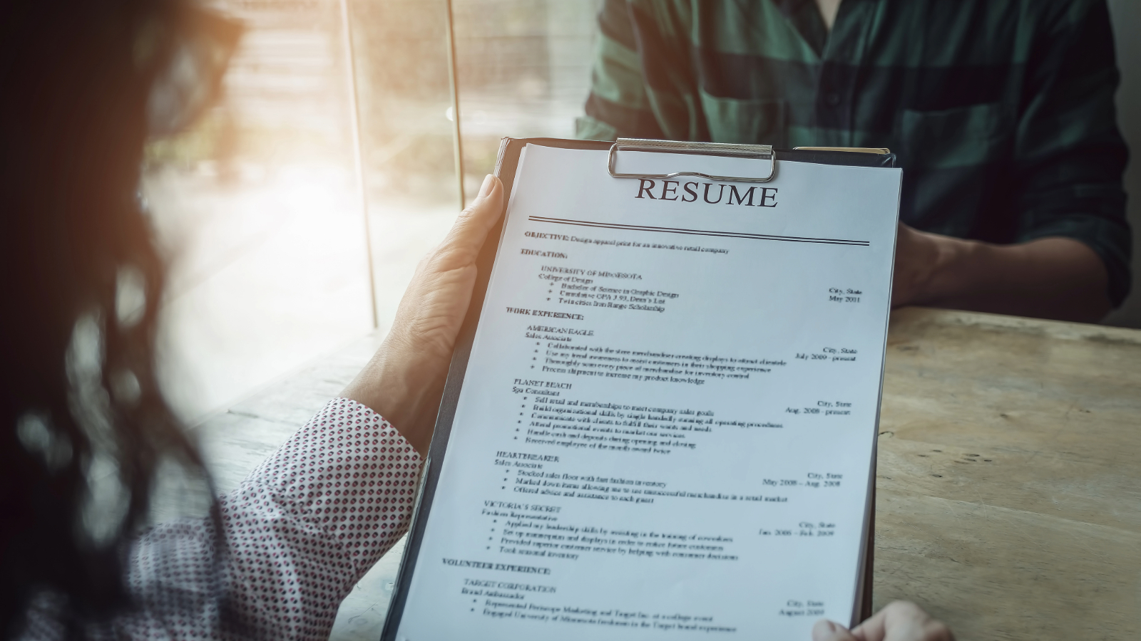 Close up photo of a hiring manager looking at a resume sitting across from a job candidate.
