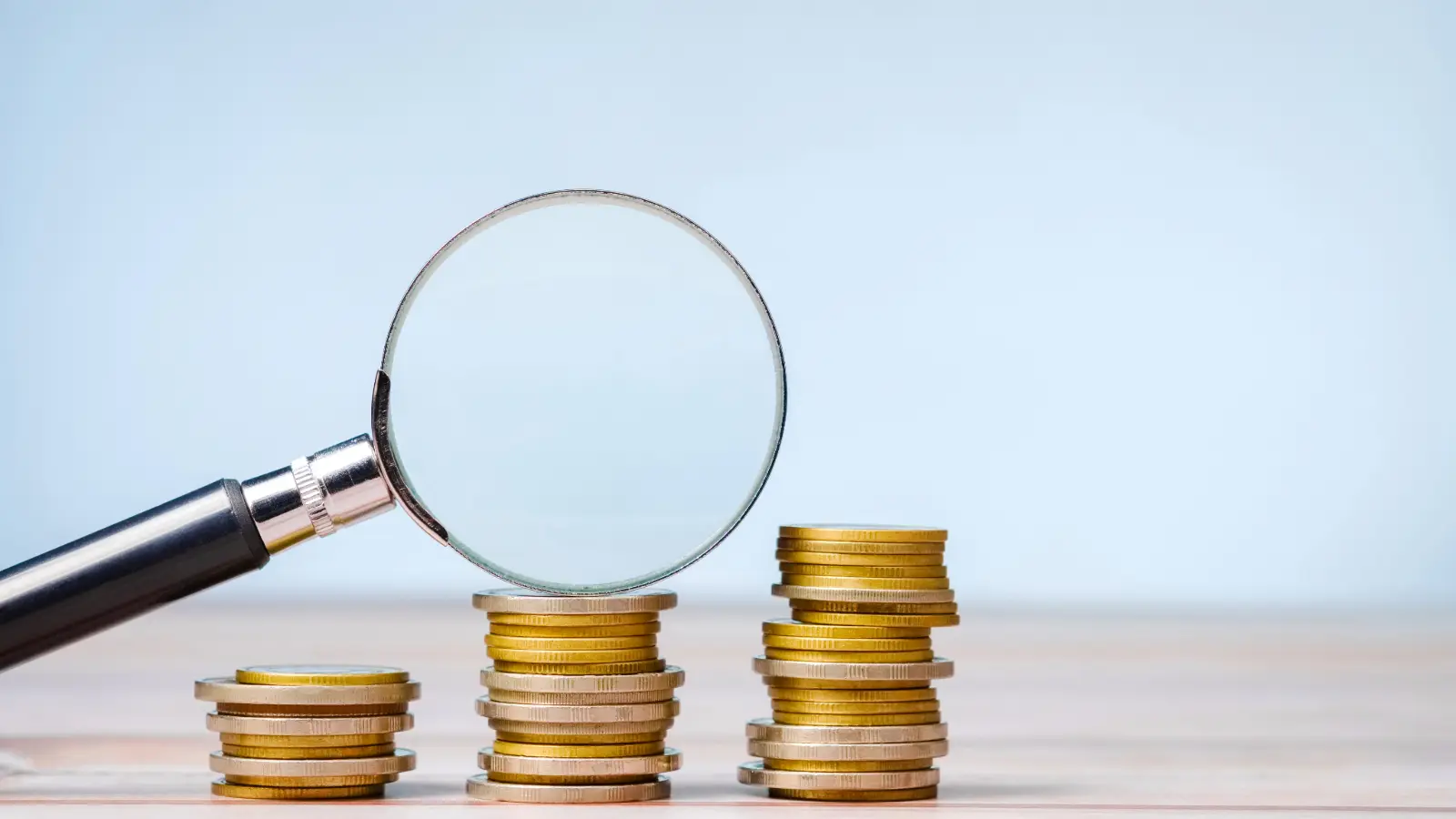A magnifying glass propped against three stacks of coins.