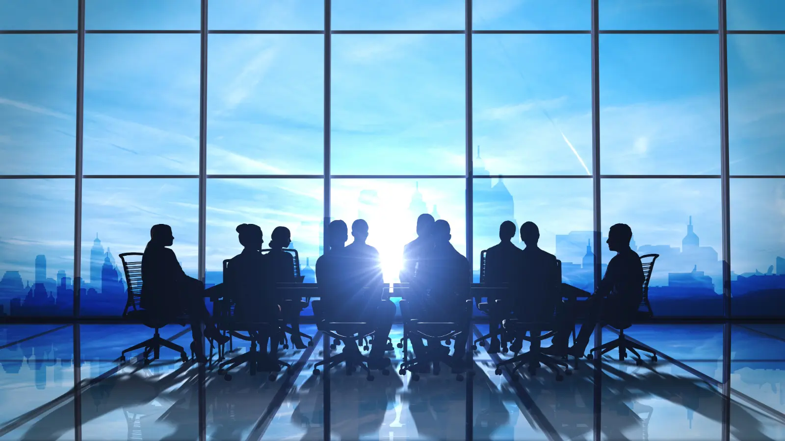 A group of executives sitting at a conference table in front of a large office window at sunset.